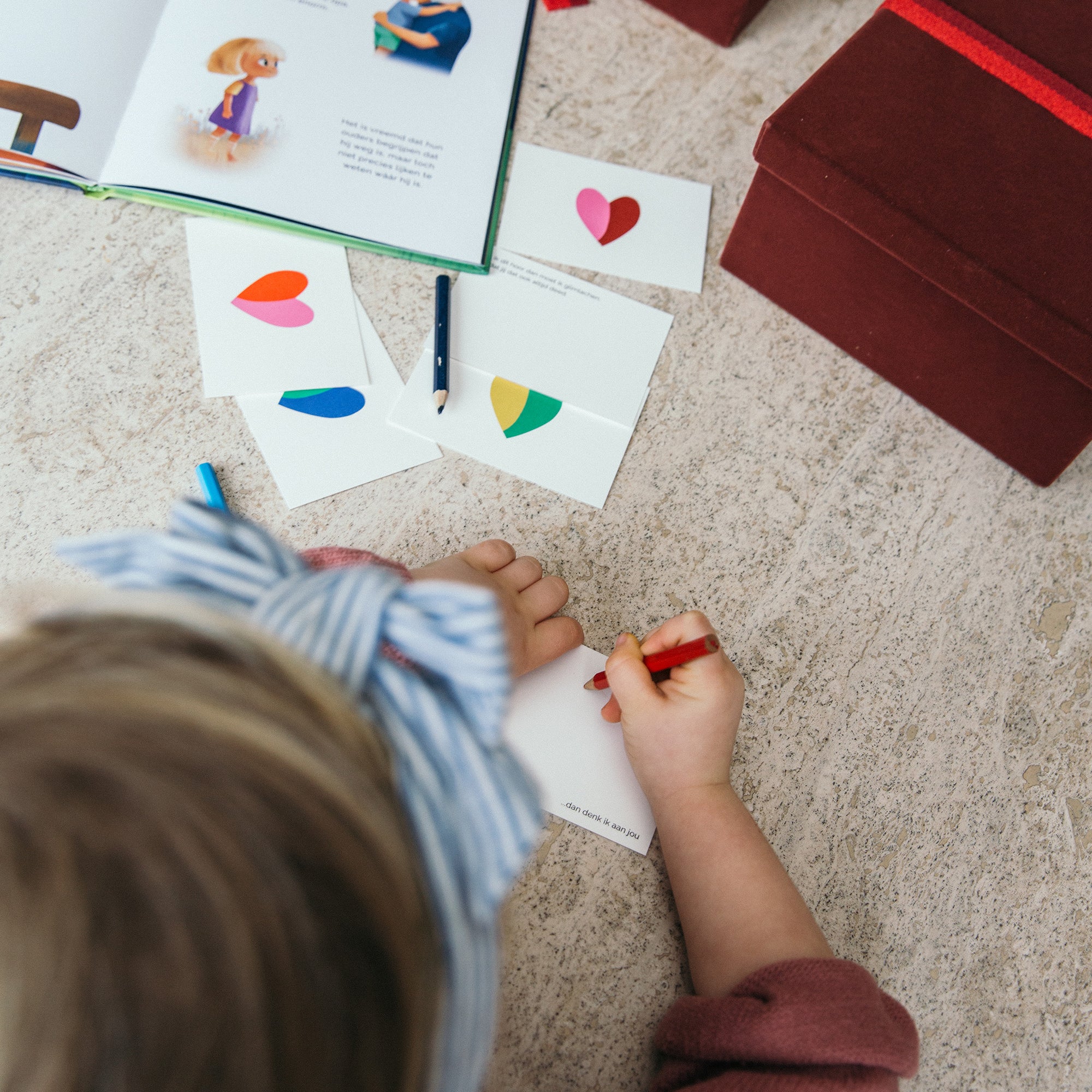 Kind tekent op een 'Thinking of You' wenskaart, met de 'Waar is Epi?' boeken en de Life. Archive Herinneringendoos op de achtergrond.